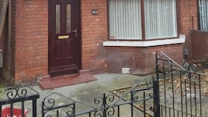 A two-story brick house with a dark brown front door, a small porch, and a metal gate. - Alexandra Park Guest House (Belfast)