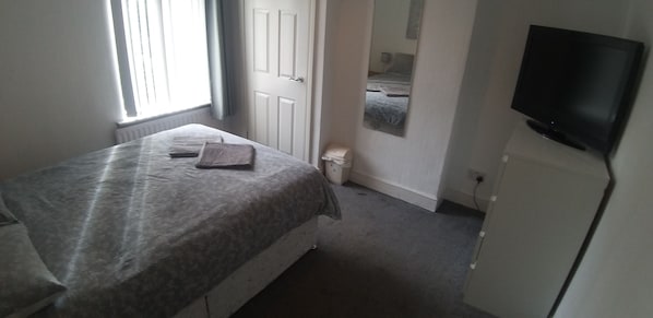 A bedroom with a bed, a television, a radiator, and a door. - Alexandra Park Guest House (Belfast)