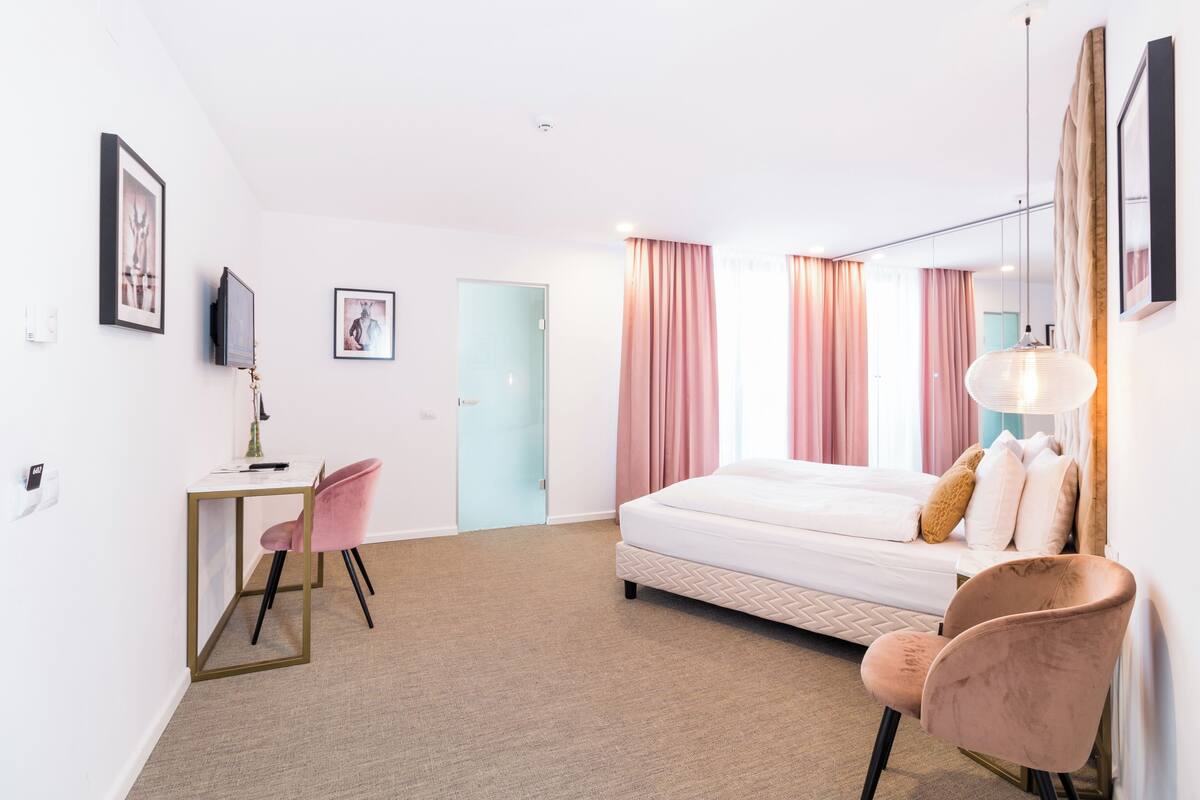 A hotel room with a bed, desk, chair, and a door.