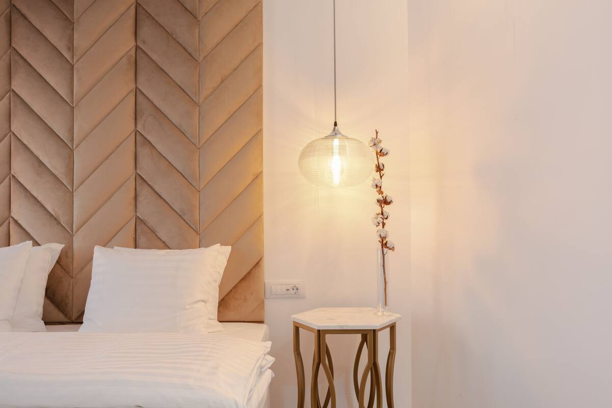 A neatly made bed with white linens, a wooden herringbone headboard, and a bedside table with a clear vase of flowers.