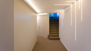 Un pasillo moderno con piso alfombrado, una escalera e iluminación empotrada.