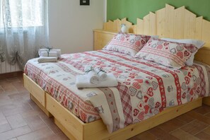 A wooden bed with a red and white patterned bedspread, a wooden headboard, and a bedside table with a lamp. - B&B Al Riparo (Finale Ligure)