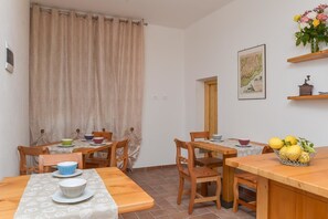 A dining area with wooden tables and chairs, a curtain, a wall-mounted picture, and a fruit basket. - B&B Al Riparo (Finale Ligure)