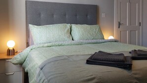 A neatly made bed with a grey headboard, green patterned bedding, and two bedside lamps. - Lawnbrook Town Guest House (Belfast)