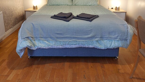 A neatly made bed with a grey headboard, two bedside tables with lamps, and a wooden floor. - Lawnbrook Town Guest House (Belfast)