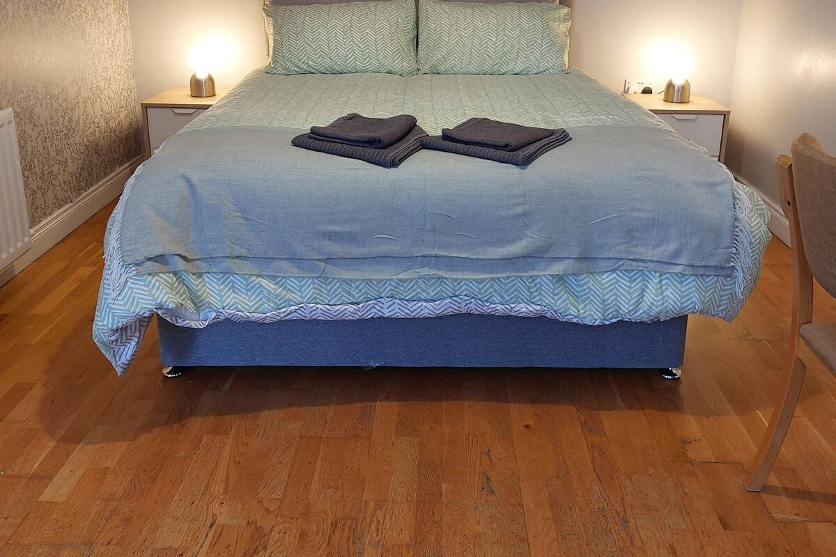 A neatly made bed with a grey headboard, two bedside tables with lamps, and a wooden floor.