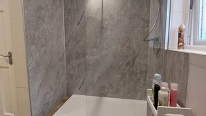 A shower with a glass door, a wooden floor, and a shelf with toiletries. - Lawnbrook Town Guest House (Belfast)