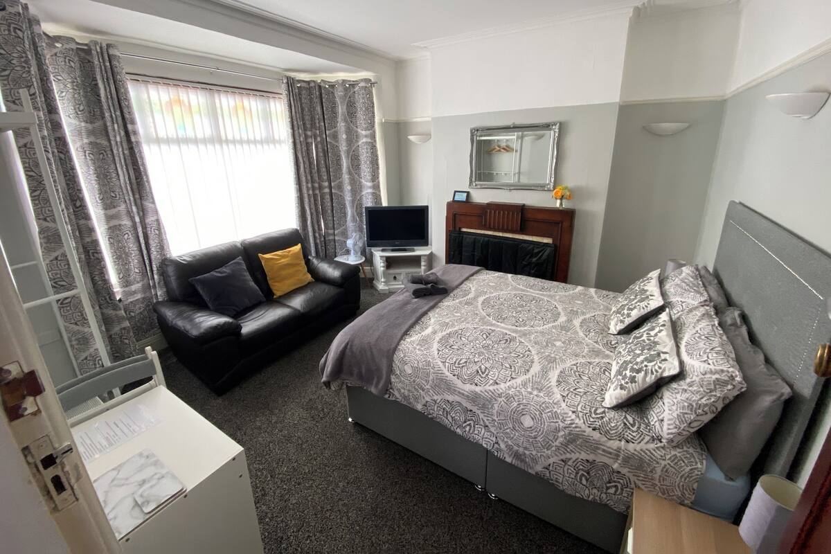 A hotel room with a bed, a sofa, a TV, a desk, and a mirror.