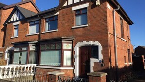 A two-story brick house with a prominent front door, a bay window, and a small porch with a metal railing. - Crumlin Road Guesthouse (Belfast)