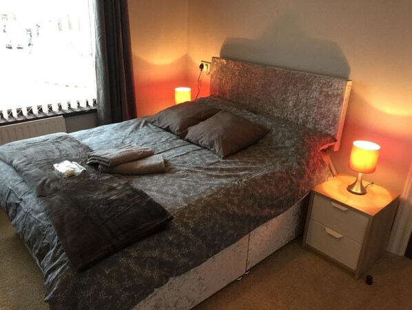 A bed with a headboard, two bedside lamps, a nightstand, and a window with blinds. - Crumlin Road Guesthouse (Belfast)