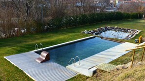 En rektangulär swimmingpool med ett trädäck, ett litet vattenfall och en bassäng av sten.