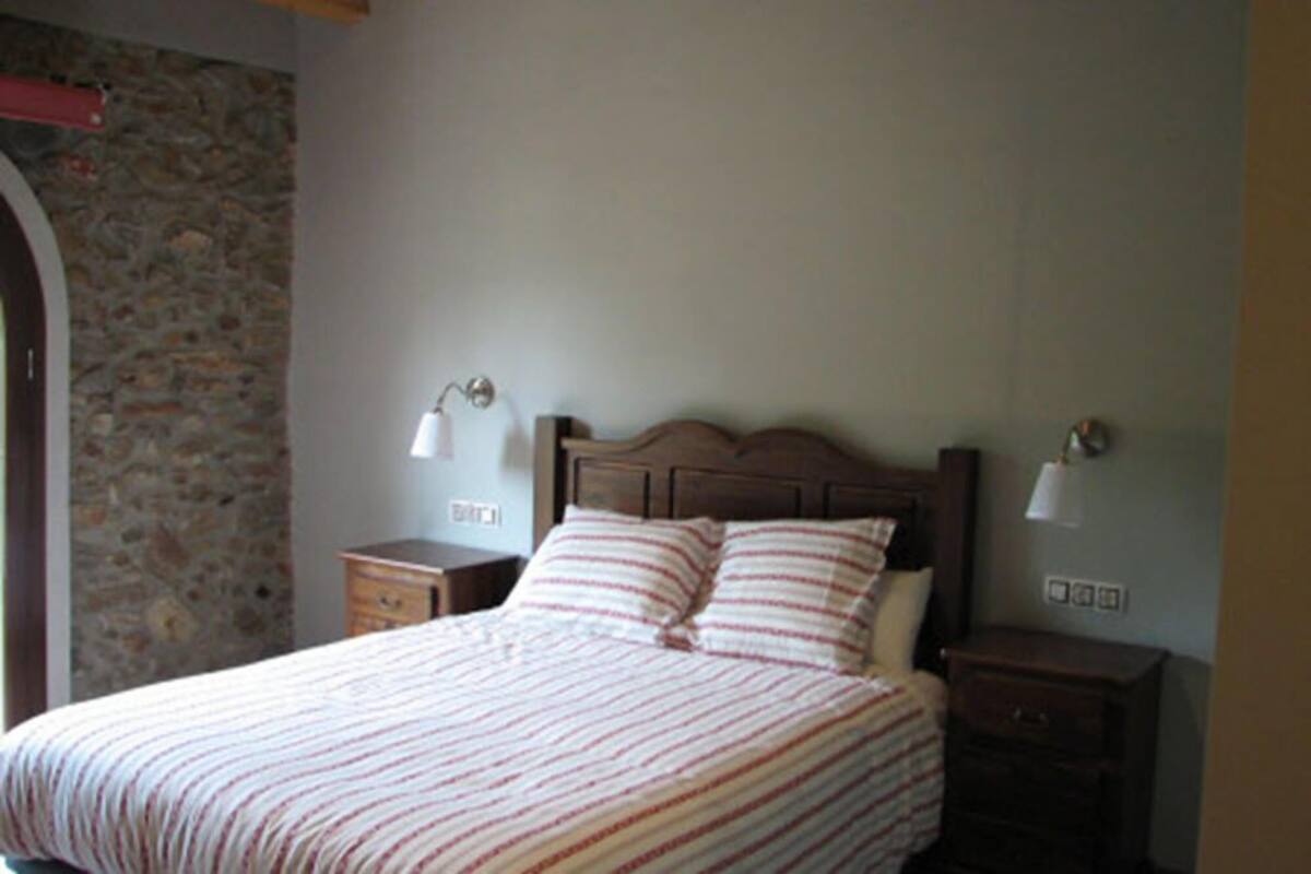 Un dormitorio con una cama, dos mesitas de noche y una pared de piedra.
