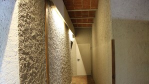 En smal hall med väggar som har en tydlig struktur och ett klinkergolv, som leder fram till en dörr.