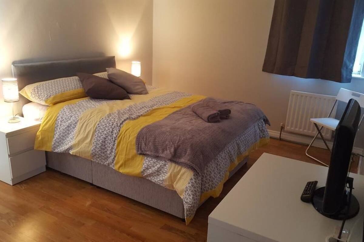 A neatly made bed with a patterned blanket, a bedside lamp, and a remote control on a white nightstand.