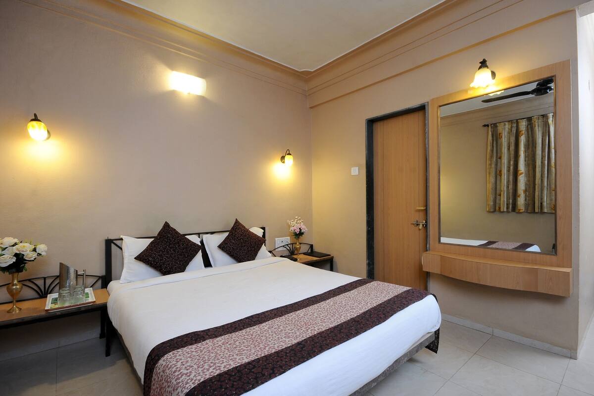 A hotel room with a large bed, two bedside tables with lamps, a mirror above the bed, and a wooden door.
