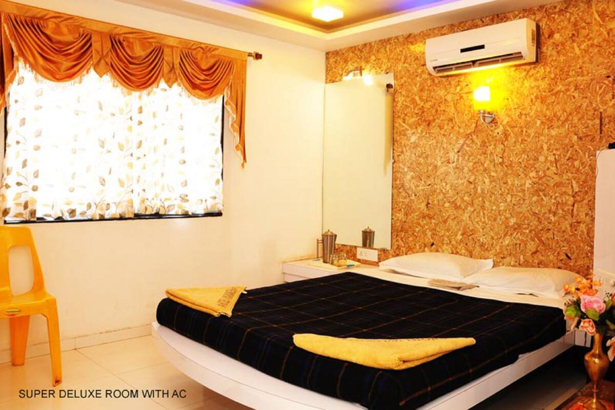 A room with a bed, a nightstand, a mirror, an air conditioner, and a window with curtains.