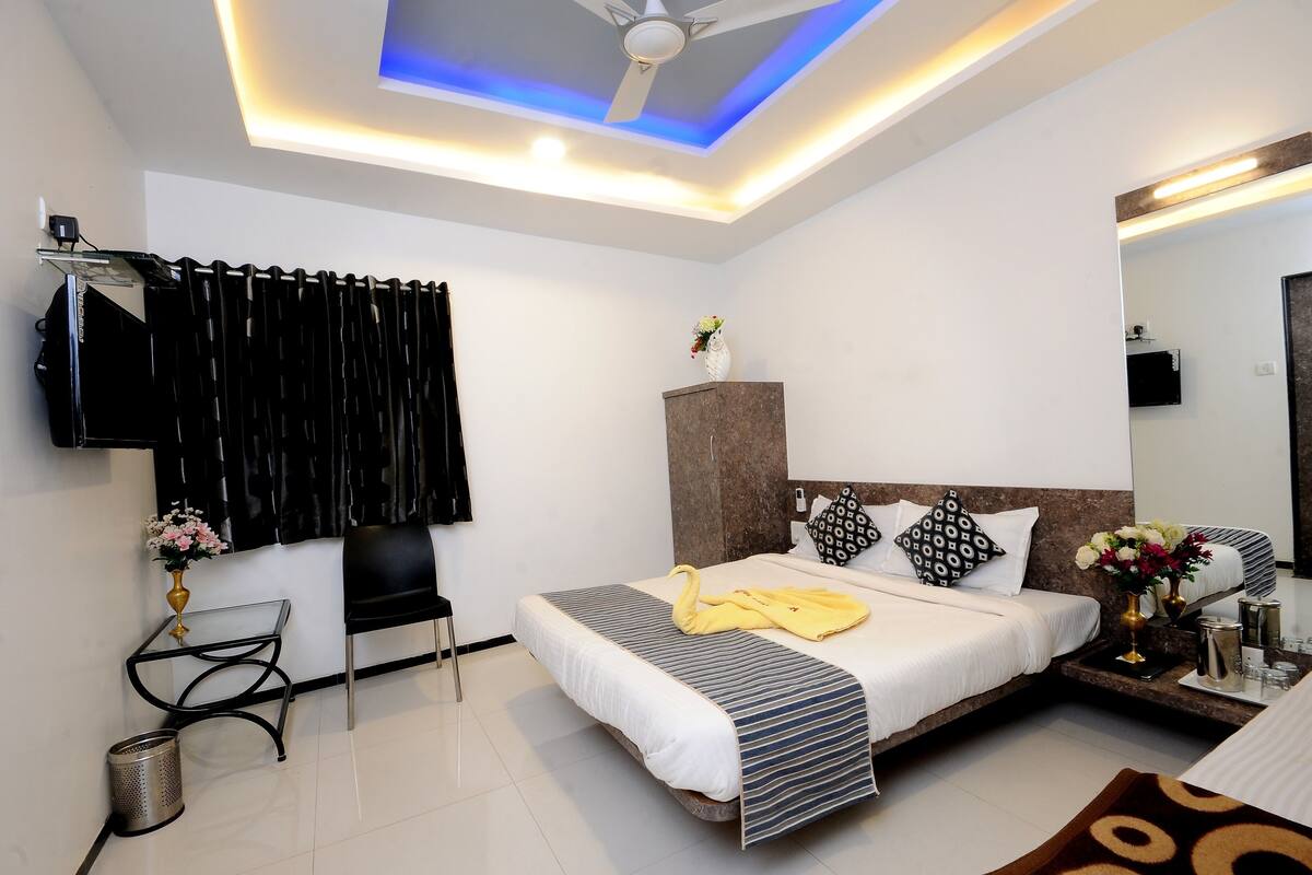 A hotel room with a bed, a desk, a chair, a TV, and a ceiling light.
