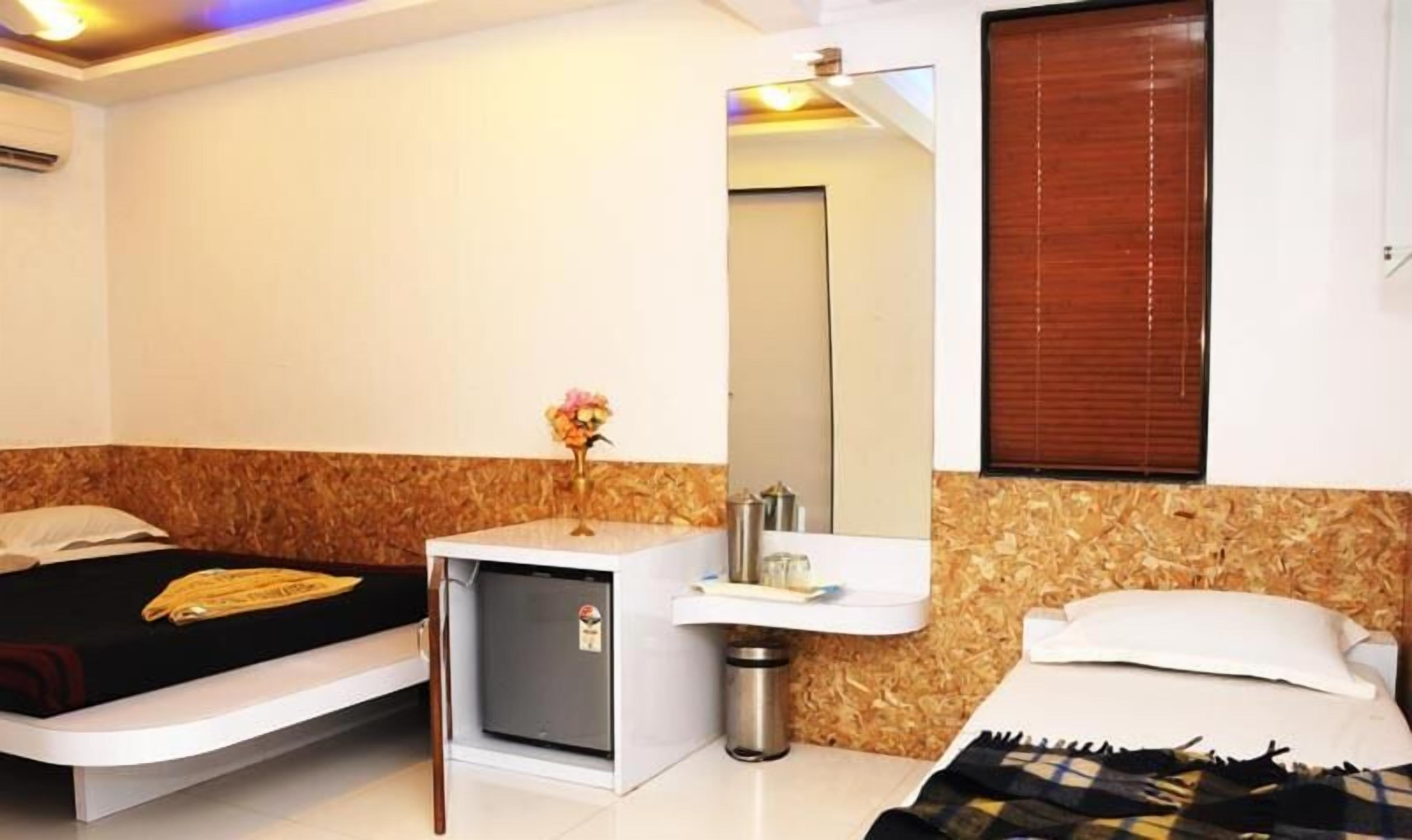 A hotel room with a bed, a small bedside table with a vase of flowers, a sink, and a mirror.