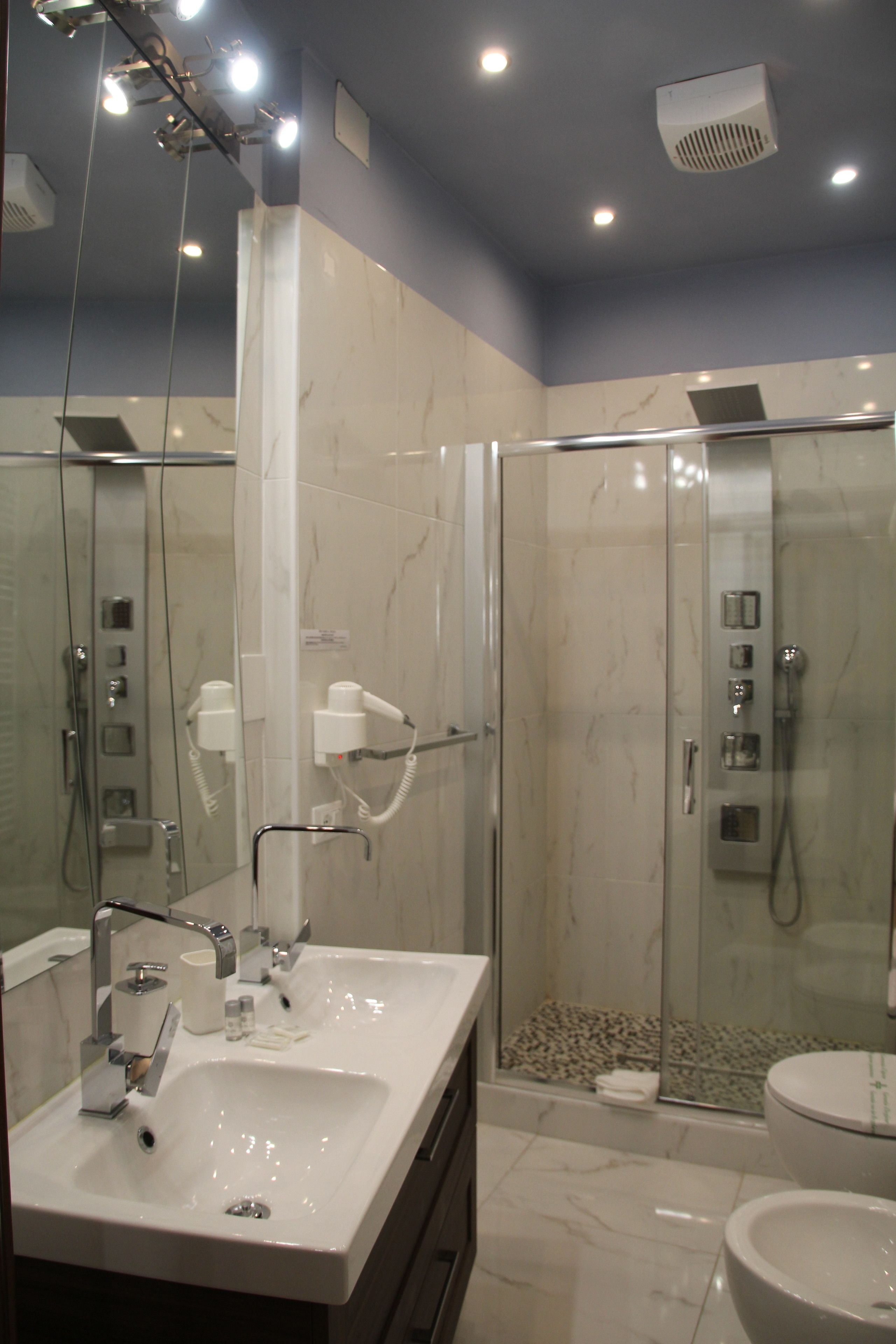 A modern bathroom with a glass-enclosed shower, a large mirror, and a white sink.