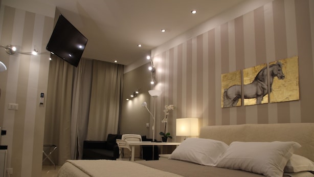 Una habitación de hotel con una cama grande, un escritorio, una silla, un televisor montado en la pared y un cuadro de un caballo.