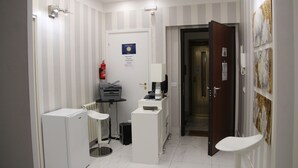 Baño de hotel con lavamanos blanco, espejo, una mesita con una impresora y puerta que da a otra habitación.