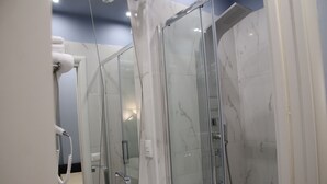 Un baño moderno con cabina de ducha de vidrio, lavamanos empotrado y secador de pelo fijado a la pared.