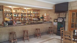 A bar area with wooden stools, a counter with various bottles, and a television mounted on the wall. - Hotel Rural Puerta De Caderechas (Oña)