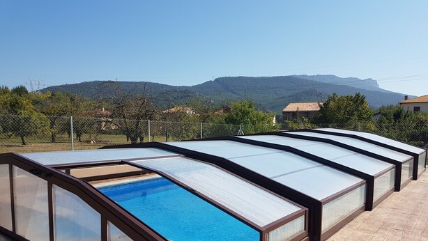 A swimming pool with glass panels and a wooden deck, surrounded by a fence and trees, with mountains in the background. - Hotel Rural Puerta De Caderechas (Oña)
