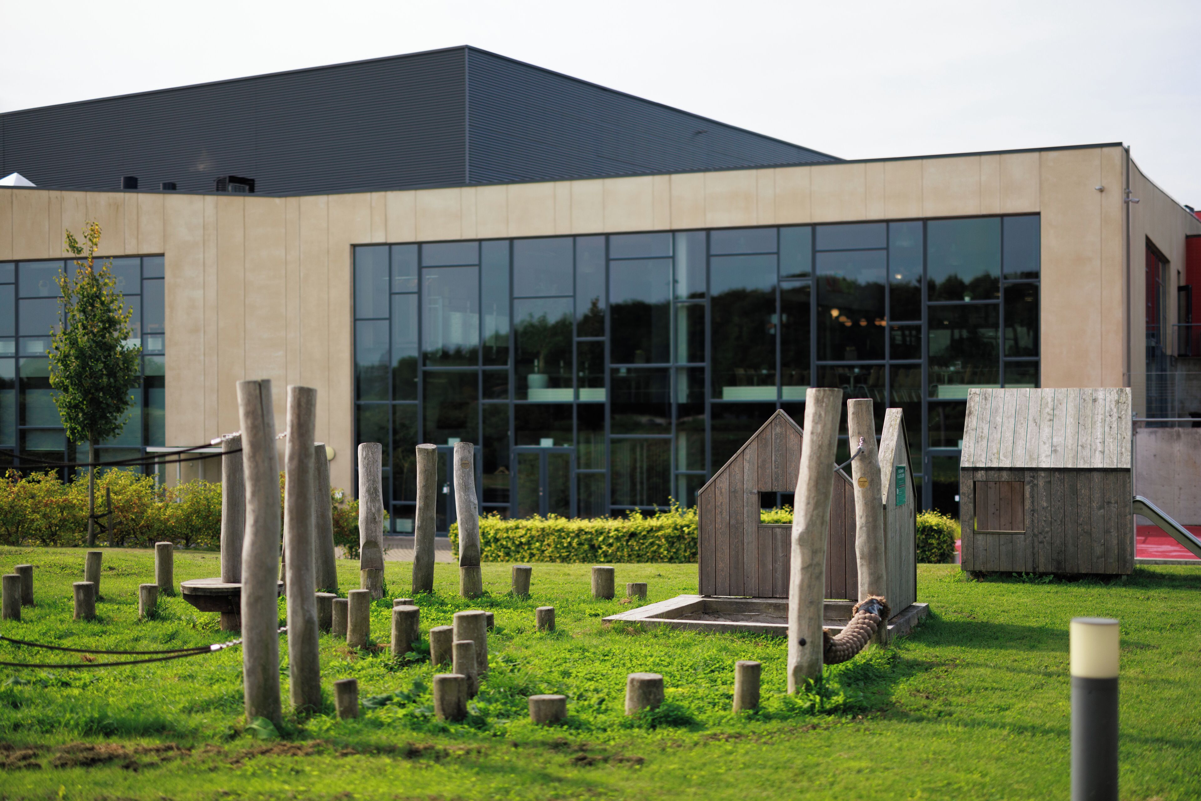 Un edificio moderno con ampie vetrate e un'area verde con pali di legno.