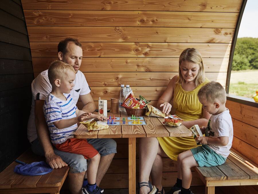 A family of four seated at a wooden table with snacks and drinks, in a wooden cabin-like setting.