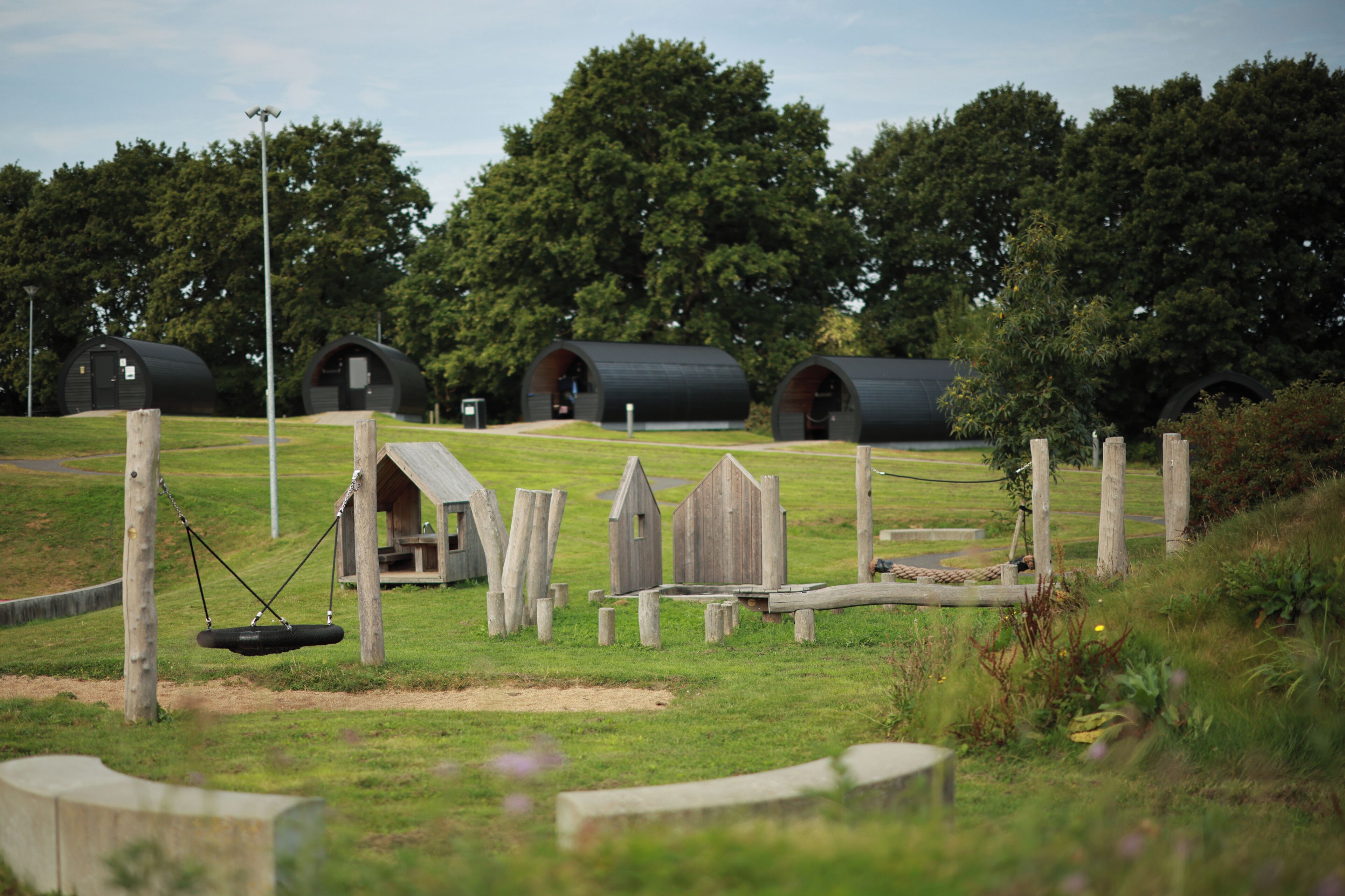 A rural setting with multiple cylindrical structures, possibly yurts, surrounded by wooden fences and a swing set.