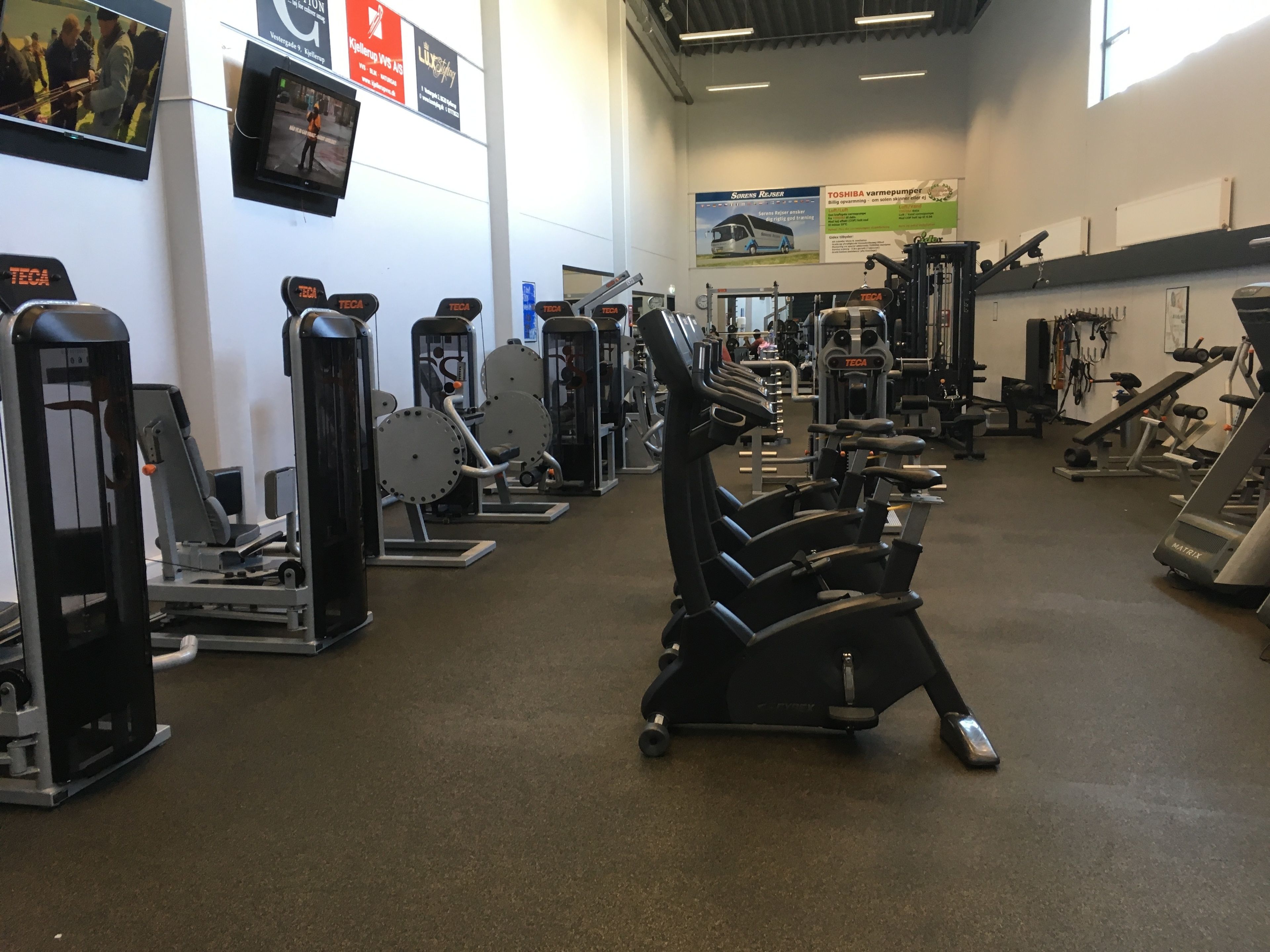 Una palestra con diverse attrezzature per l'allenamento, tra cui macchinari cardio e aree dedicate al sollevamento pesi.