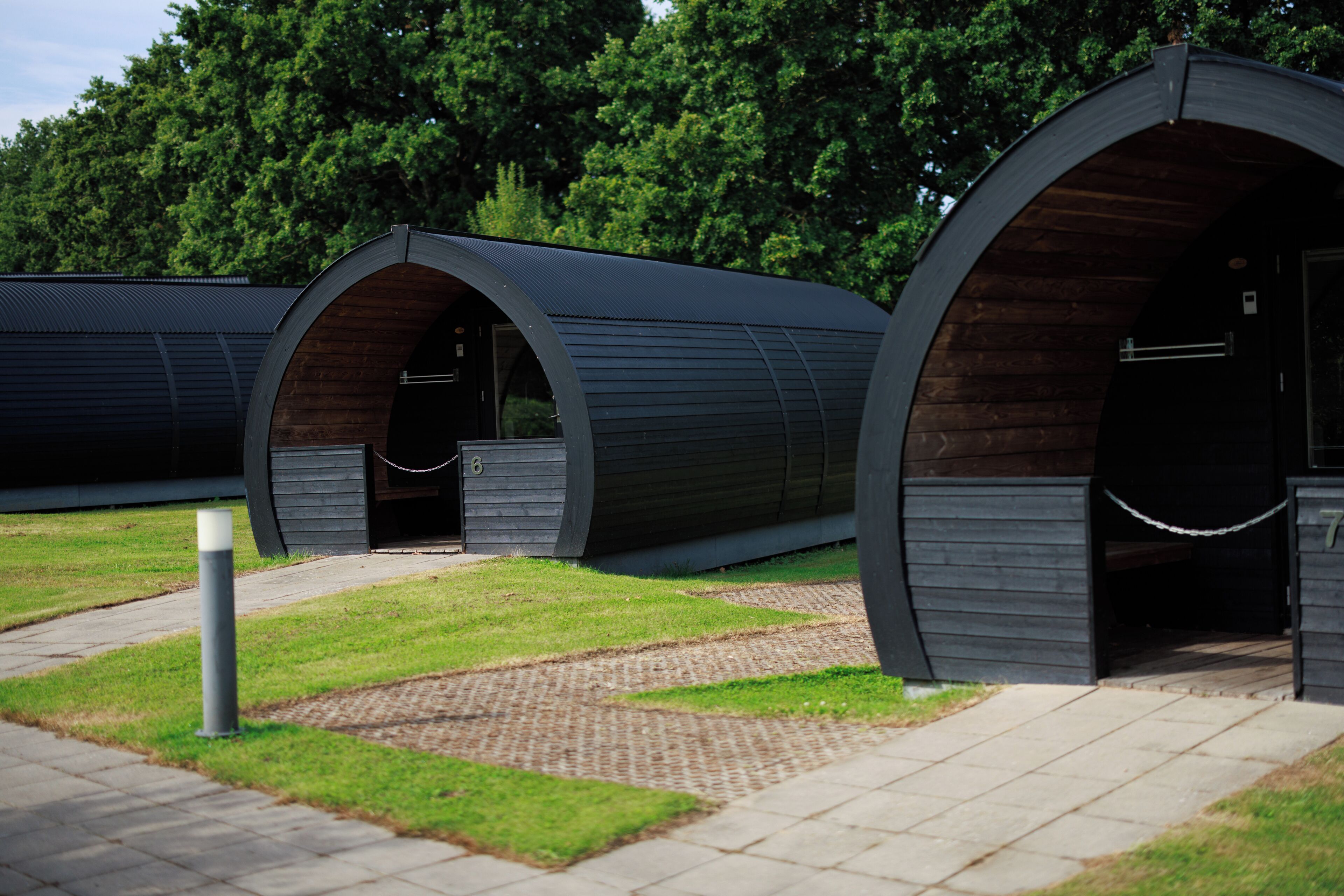 A row of modern, semi-open structures with a metal exterior and wooden interior, connected by a pathway.
