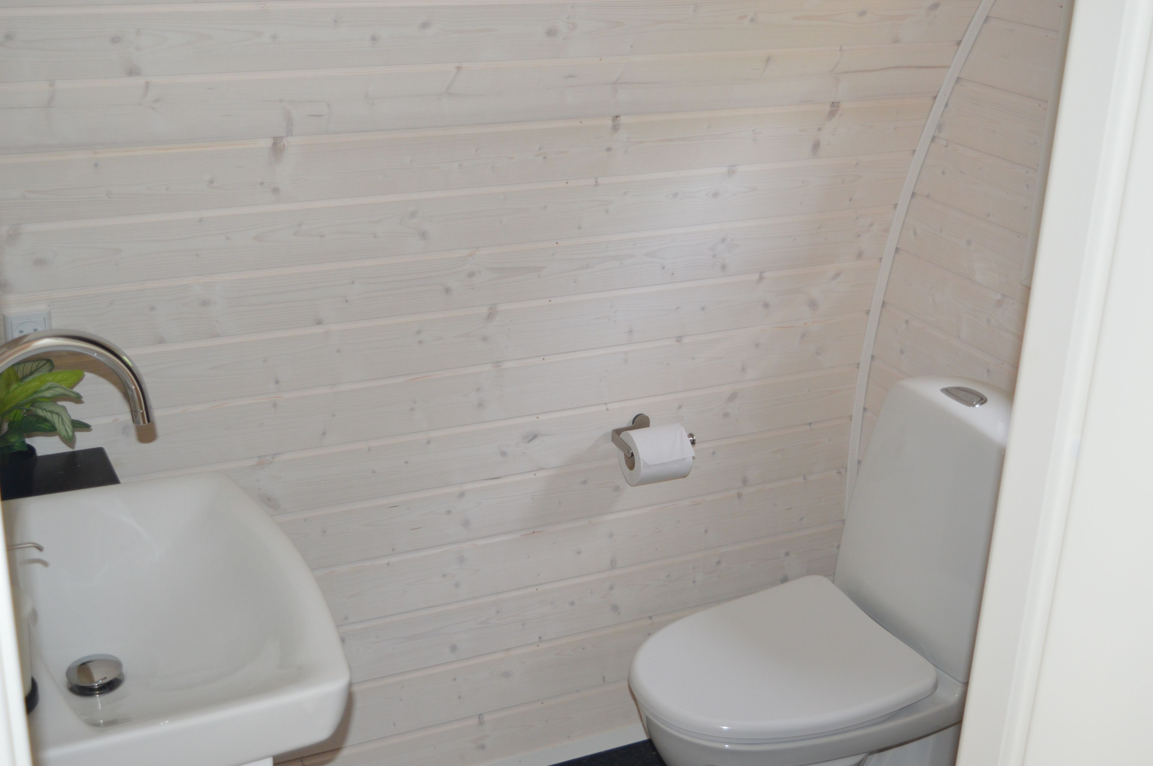 A small bathroom with a white sink, toilet, and wooden wall paneling.