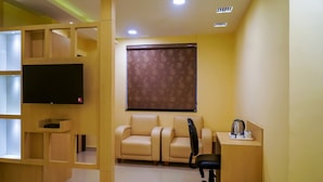 A modern room with a flat-screen TV, a sofa, a desk with a chair, and a window with a patterned blind. - Treebo Oasis, Laxmisagar (Bhubaneshwar)