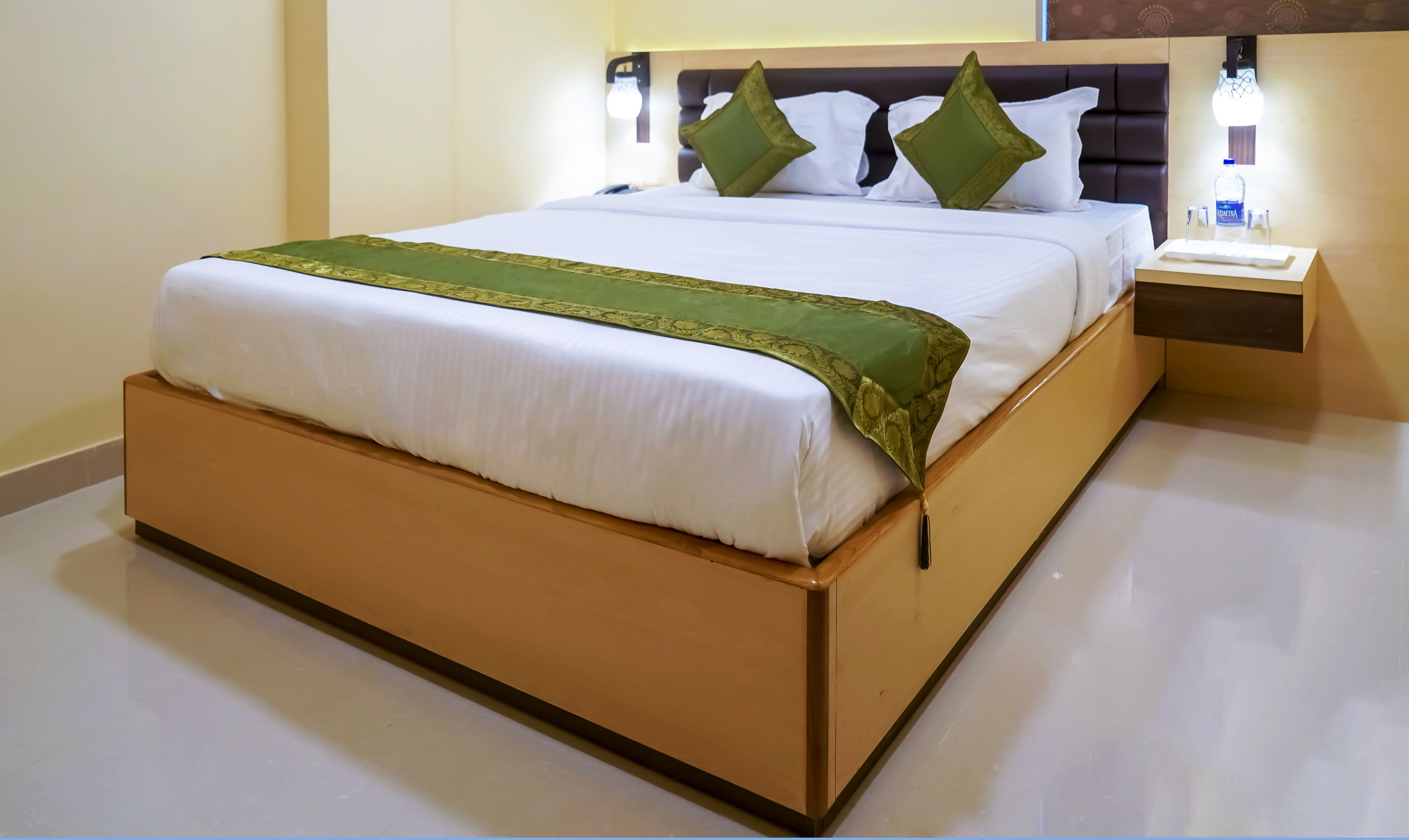 A neatly made bed with a green bedspread and a white comforter, a wooden headboard, and a bedside table with a lamp.