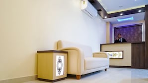 A reception area with a beige sofa, a wooden side table, and a reception desk with a decorative mirror. - Treebo Oasis, Laxmisagar (Bhubaneshwar)