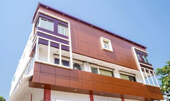 A multi-story building with a modern architectural design, featuring a combination of white and brown panels, large windows, and a flat roof.