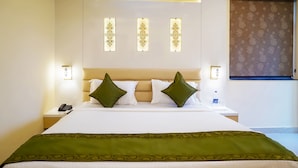 A hotel room with a bed, green pillows, a green bedspread, a nightstand with a phone, and wall sconces. - Treebo Oasis, Laxmisagar (Bhubaneshwar)