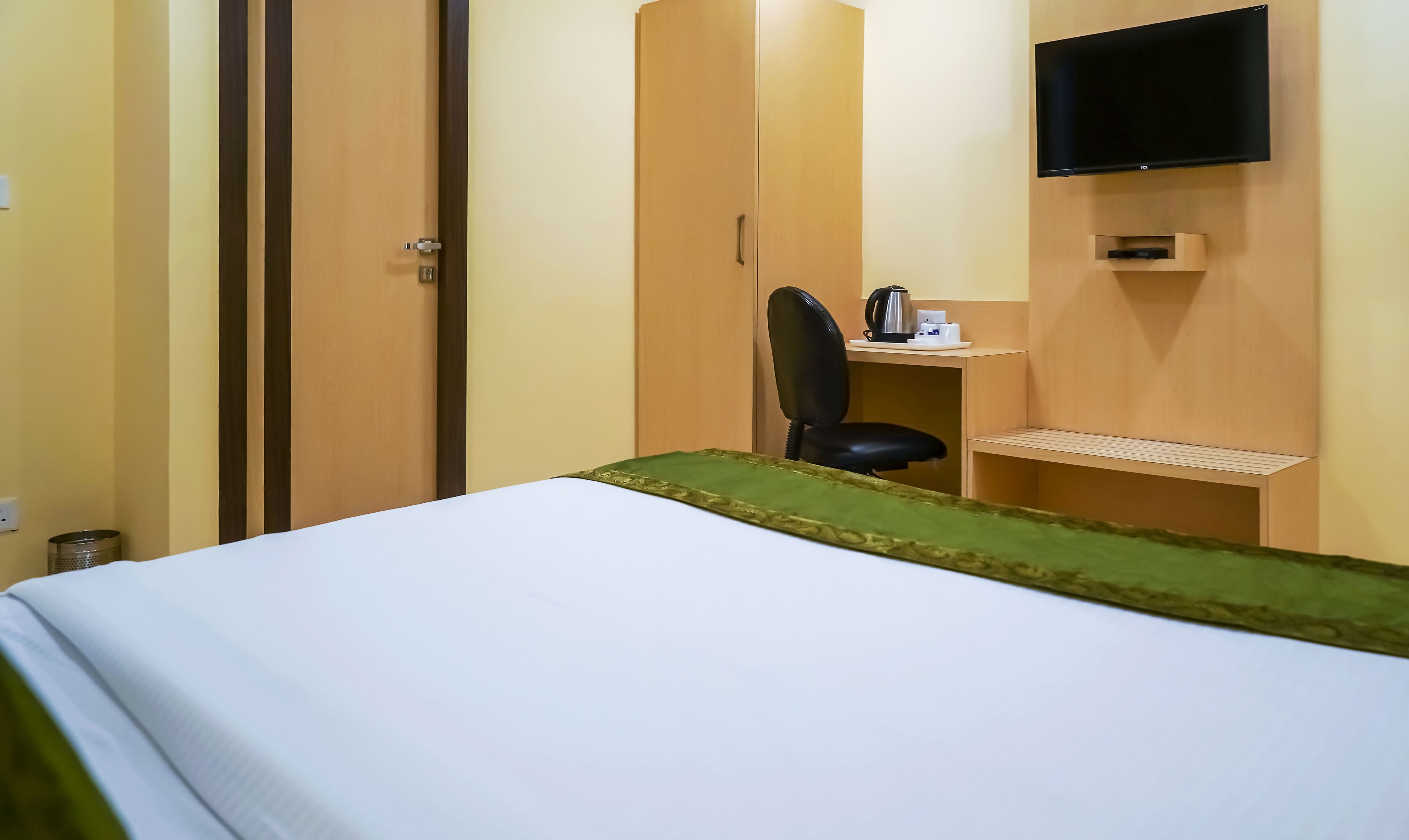 Et hotelværelse med en seng, et skrivebord med stol, et fjernsyn og et klædeskab.