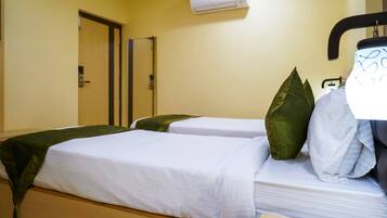 A hotel room with two beds, each with white linens and green pillows. There is a door and an air conditioning unit on the wall.