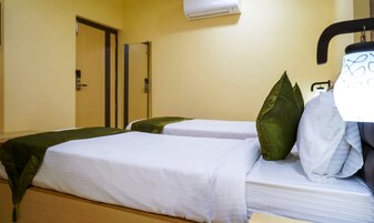 A hotel room with two beds, each with white linens and green pillows. There is a door and an air conditioning unit on the wall.