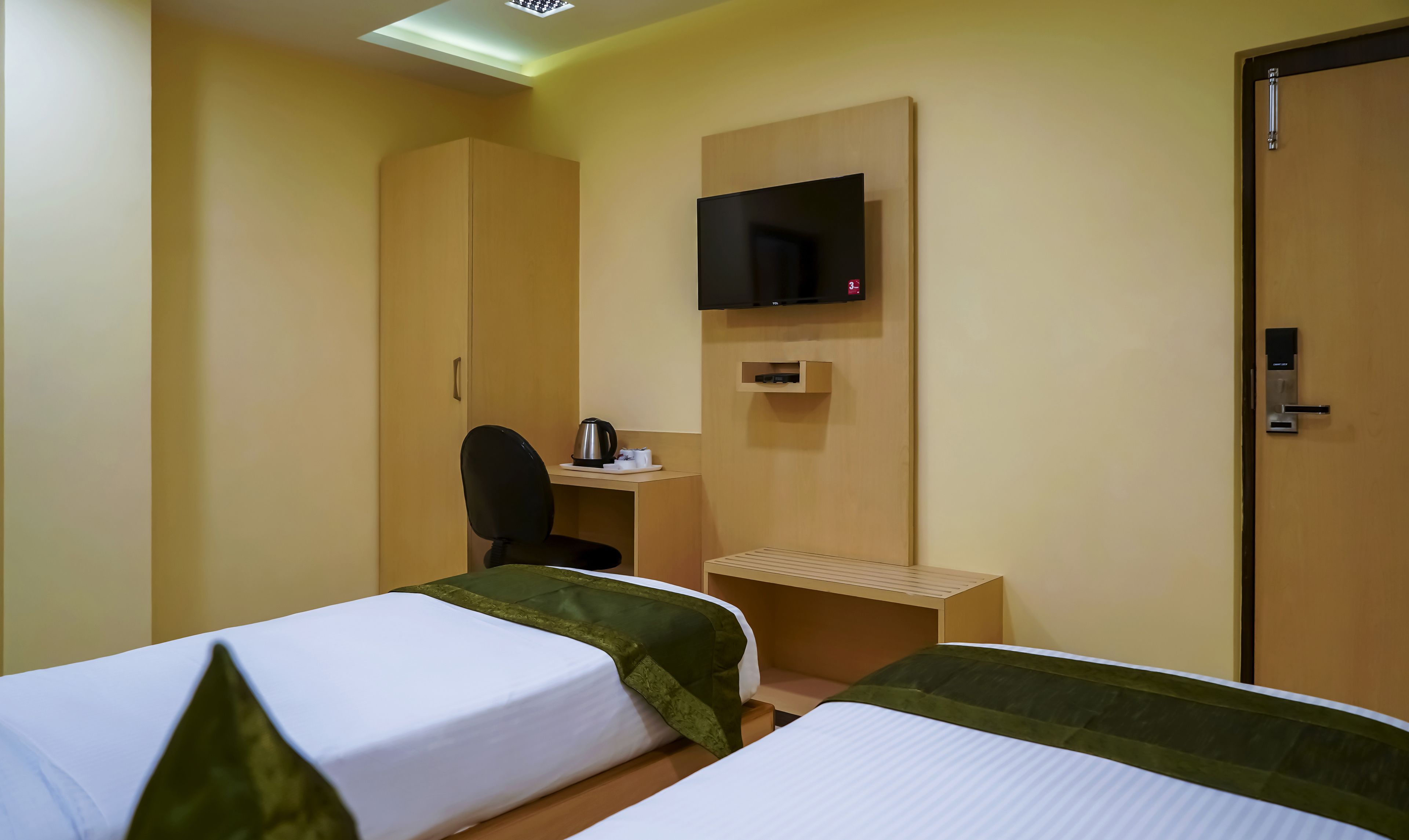 Habitación de hotel con dos camas, un escritorio, una silla, un televisor montado en la pared y una puerta.
