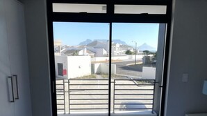 A bedroom with a bed, a window, and a view of buildings and mountains. - Two Bedroom Apartment (Cape Town)