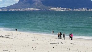 A beach with a kite flying, a mountain in the background, and people on the shore. - Two Bedroom Apartment (Cape Town)