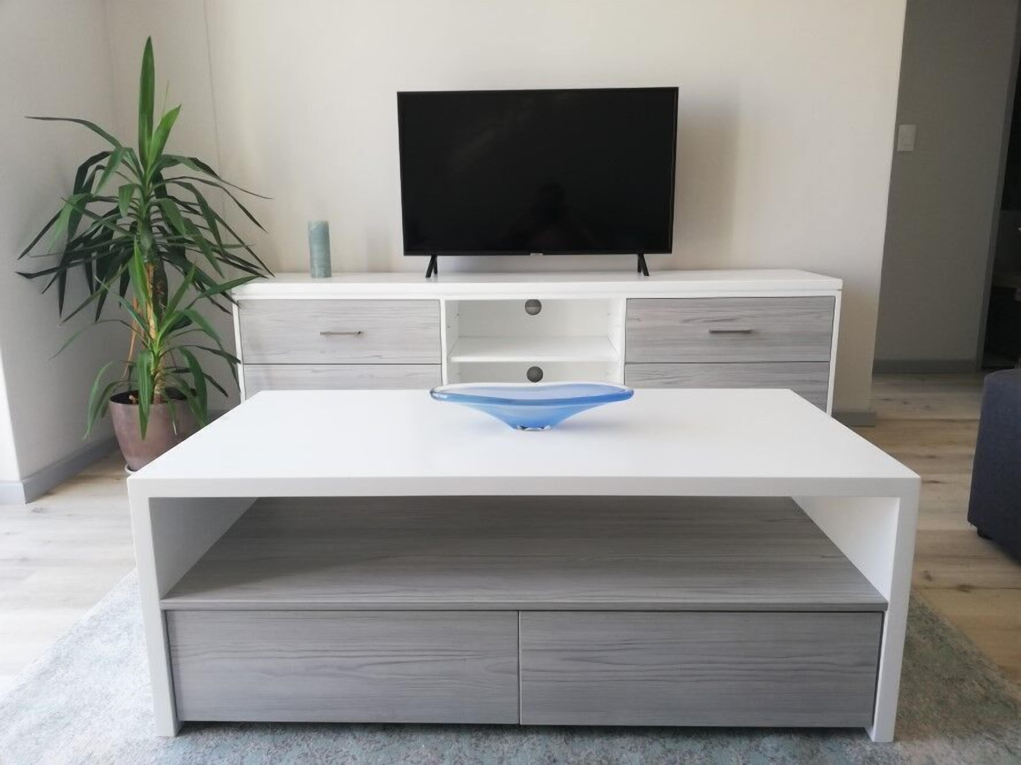Ein modernes Wohnzimmer mit einem weißen TV-Schrank, einem blauen Glastisch und einem Blumentopf.