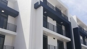 A modern multi-story building with white and dark accents, featuring balconies with metal railings. - Two Bedroom Apartment (Cape Town)