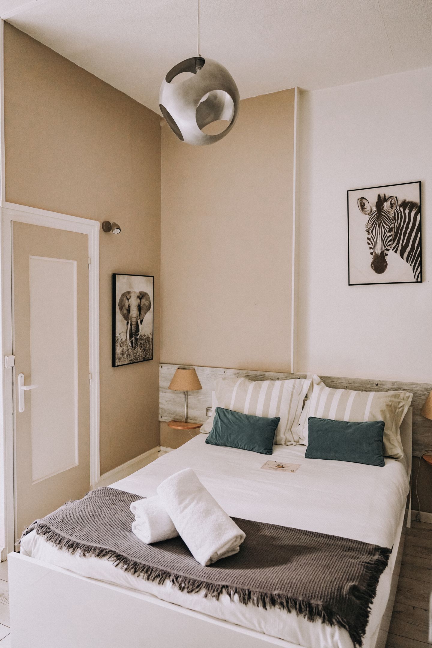 A bedroom with a bed, pillows, a blanket, a hanging light fixture, and two wall-mounted pictures.