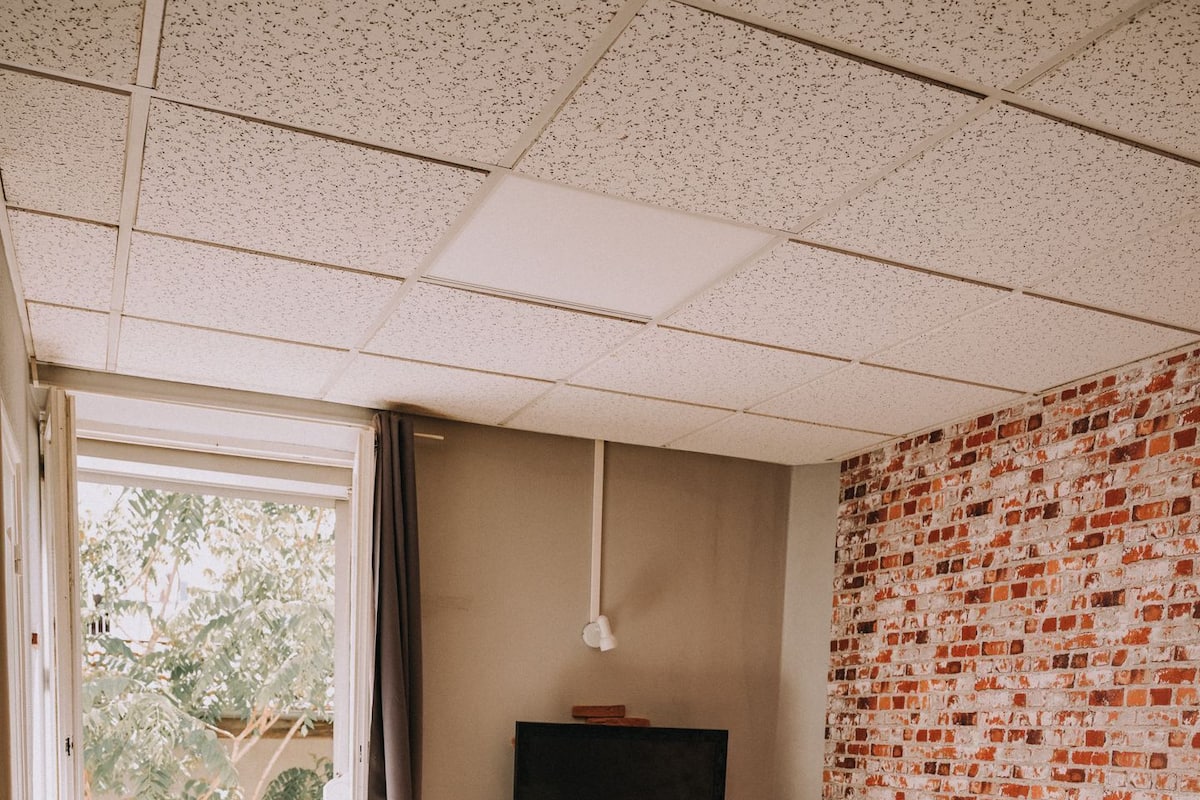Un dormitorio con cama, escritorio con computadora, televisor y ventana con cortinas.
