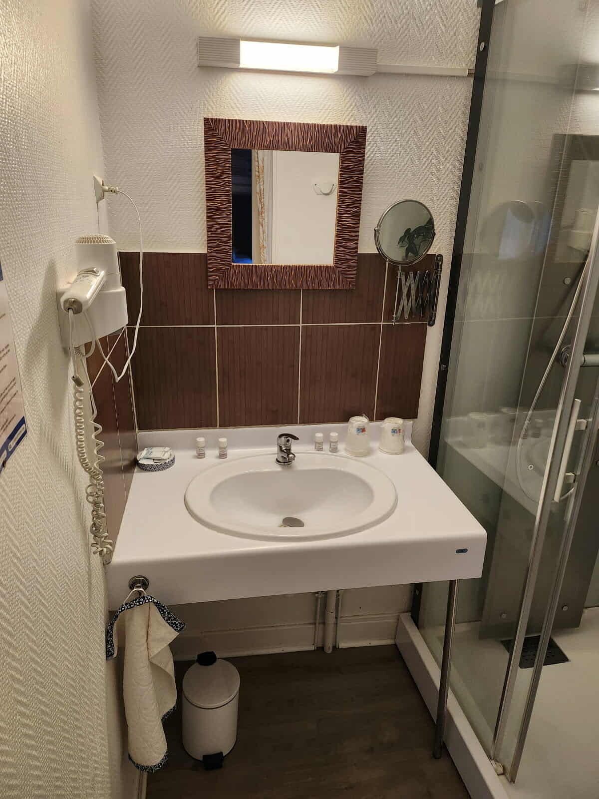 A bathroom with a white sink, a mirror, a towel rack, and a glass shower enclosure.